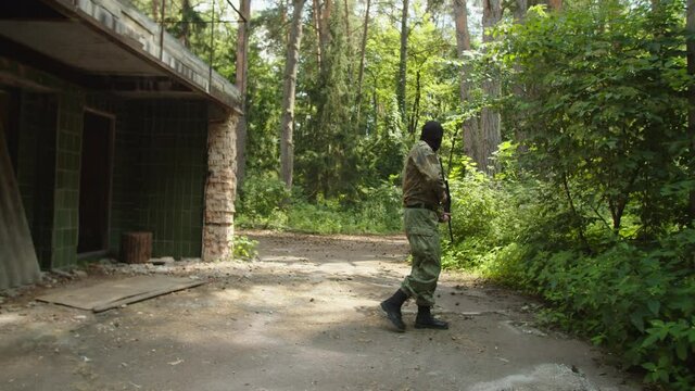 Anti-terrorist mission by equipped professional soldiers outdoors. Counter-terrorist squad eliminating terrorist on watch, applying chokehold, hiding body around corner of abandoned building