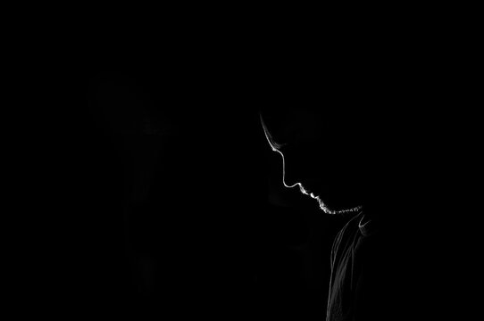 Male profile silhouette. sad or dejected young man on black background. Unrecognizable person looking down. Image with copy space.