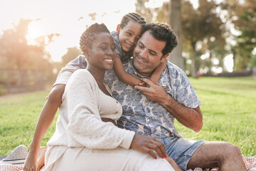 Happy multiracial family enjoy picnic at city park - African pregnant woman with caucasian husband and mixed race child outdoor