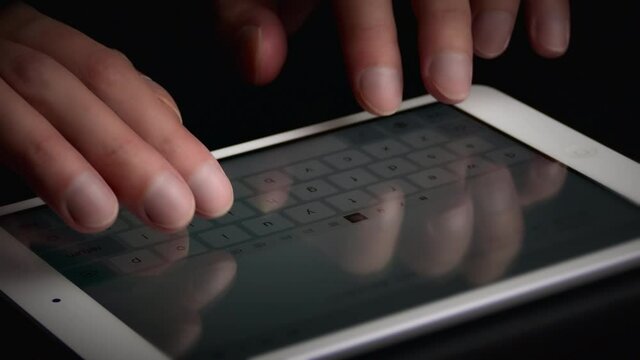 Man typing text on electronic tablet using screen keyboard. Hands close-up.
