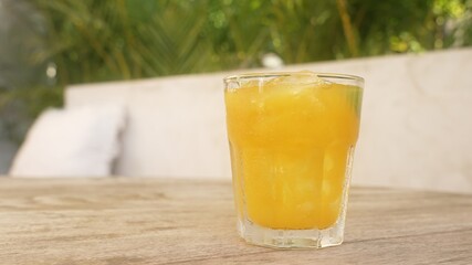 A beautiful glass glass with orange juice stands on the wooden table of the restaurant on a sunny day. A glass with a drink with a natural antibiotic Jamu on the background of a white wall of a cafe.