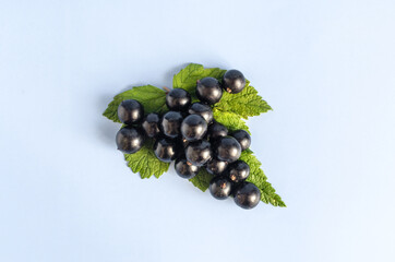 Black currant berries with green leaves on a blue background close-up. Black berries and green...