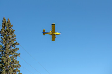 A yellow crop dusting airplane flying overhead in rural Saskatchewan, Canada.  The spray equipment is visible on the underside of the plane.
