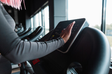 Naklejka premium Young athletic woman starts jogging on treadmill and chooses running mode