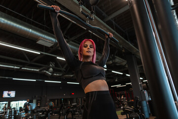 Fitness woman in black fashionable sportswear working out on the exercise machine and looking at the camera