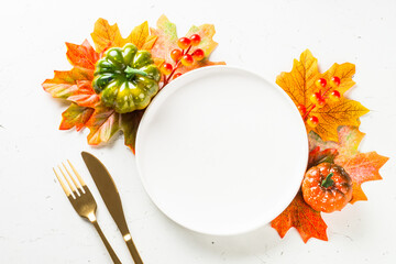 Autumn table with white plate, golden cutlery and fall leaves and decorations at white table. Top view with copy space.
