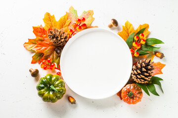 Autumn table with white plate, fall leaves and decorations at white table. Top view with copy space.