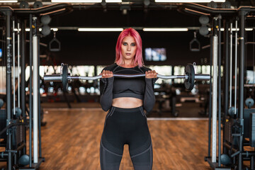 Fototapeta na wymiar Beautiful fitness model woman in black stylish sportswear workout and trains with a barbell in the gym and looks at the camera