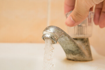 Hand holding to open the old and dirty faucet on the wash basin  and copy space