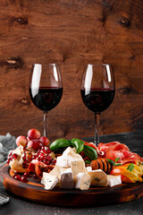  A set of appetizers for wine, jamon, pepperoni, cheese, grapes, peach and olives on the table. Snack board and two glasses of red wine vertical photo