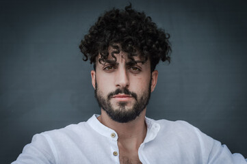 close up portrait of a young man with a beard and curly hair, looking at the camera