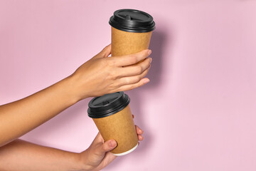 Close-up on a pink background, a woman's hand holds a paper cup with coffee in a stand. Coffee or tea to go. People hands passing one another cup of coffee, coffee delivery.