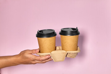 Close-up on a pink background, a woman's hand holds a paper cup with coffee in a stand. Coffee or tea to go. People hands passing one another cup of coffee, coffee delivery.