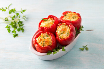 Bell red peppers stuffed with pasta, vegetables, cheese and herbs in baking dish on light blue background, top view, copy space. Delicious homemade food