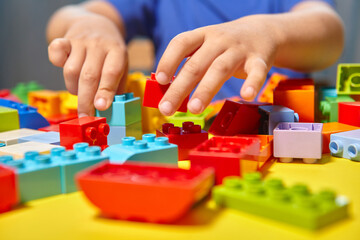 A beautiful boy is playing at home with building blocks. A cute smiling boy is playing with a constructor with a lot of colorful plastic blocks in the room, building a city. Preschool classes.