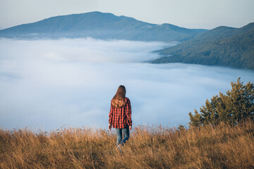 Young Girl in a Plaid Shirt in the High Mountains above the Clouds