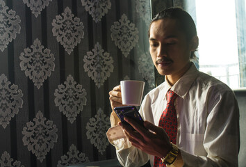Professional Asian Man drinking coffee while using a cell phone for work