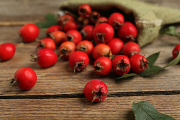 Fototapeta na wymiar Ripe rose hip berries with green leaves on wooden table, closeup
