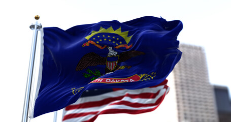Naklejka premium the flag of the US state of North Dakota waving in the wind with the American stars and stripes flag blurred in the background
