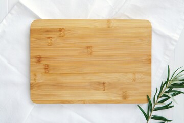 Kitchen flat lay composition, wooden cutting board mockup for engraving design, tea towel and green branch.