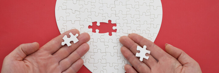 Woman and a man hand assemble jigsaw puzzle in shape of heart