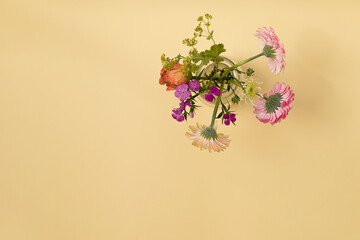A small bouquet of spring flowers in a glass vase against yellow background. Summer lay out with copy space.