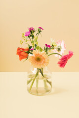 A small bouquet of spring flowers in a glass vase against yellow background. Summer lay out with...