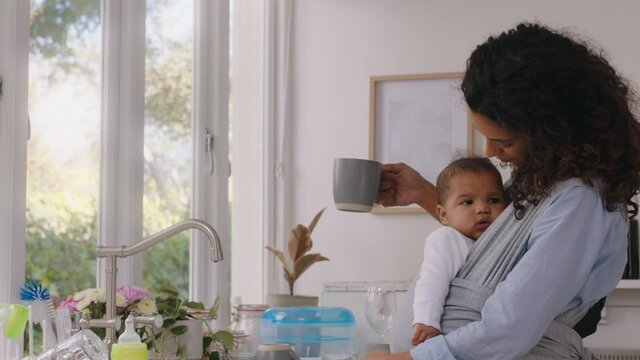 happy mother holding baby at home tired mom drinking coffee relaxing after housework washing dishes in kitchen