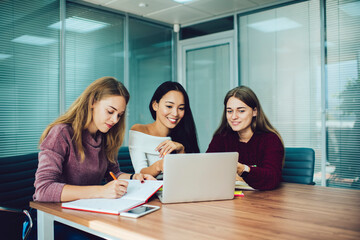 Cheerful colleagues collaborating on web startup project using netbook technology during work day in office interior, skilled employees reading news in social media while briefing at desktop