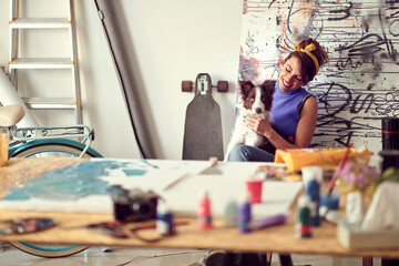 Fototapeta premium A young female artist is enjoying a break with her dog while working on a new painting in the studio. Art, painting, friendship, studio