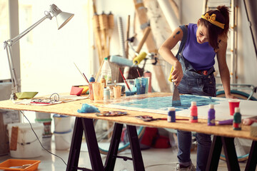 A young female artist is using a spatula to spread the paint over a new painting she is working on...