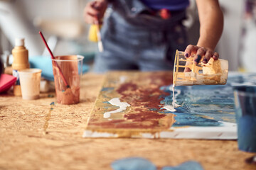 A young female artist is pouring the paint over a new painting she is working on in the studio....