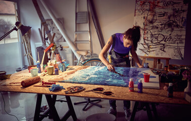 A young female artist is focused while working on a painting in the studio. Art, painting, studio - obrazy, fototapety, plakaty