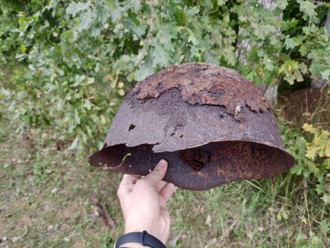 White caucasian male hand holding old rusted World War 2 soviet helmet. Forest background