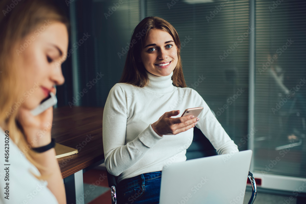 Poster portrait of cheerful female it professional with modern laptop computer and smartphone device smilin