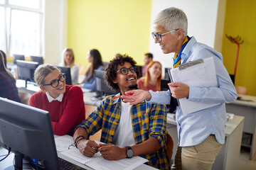 A female professor evaluating work of students at the informatics lecture. Smart young people study at the college. Education, college, university, learning and multiethnic people concept