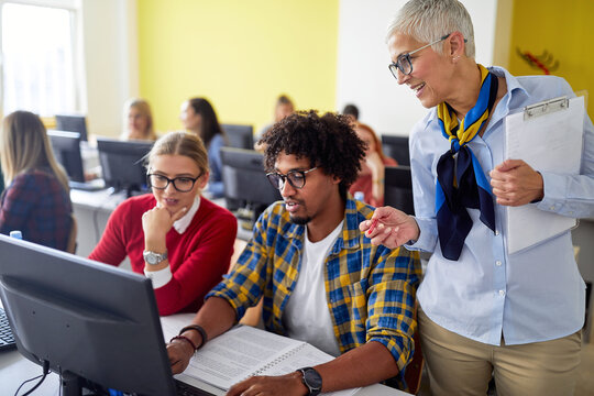 A female professor checking work of students at the informatics lecture. Smart young people study at the college. Education, college, university, learning and multiethnic people concept