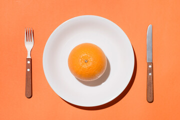 Top view of orange fruit on white plate with knife and fork on orange background