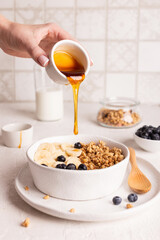 Woman adds honey to granola, healthy breakfast with muesli and fruits