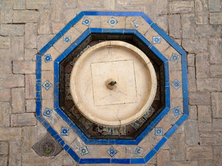 Aerial view of a fountain basin made of marble, inserted on a brick ground and surrounded by a blue...