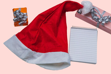 Close up view of red Santa hat, pen, gift box and notebook on pink background. Christmas concept. Sweden. 