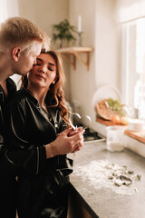 A happy man and a woman in love in pajamas hug, kiss and cook a romantic dinner together in a decorated kitchen in a cozy eco-style country house in the winter Christmas holidays, selective focus