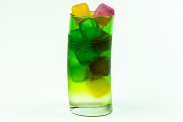 Colorful ice cubes and water in green glass cup on white background