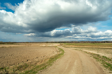 Fototapeta na wymiar A sandy road through the fields and clouds on the sky
