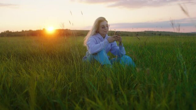 Smiling large charismatic woman enjoy the time at nature take sit down in the grass in the middle of a large field she typing something on her smartphone concentrated
