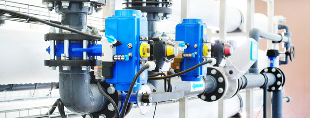 Large industrial water treatment and boiler room. Shiny steel metal pipes and blue pumps and...
