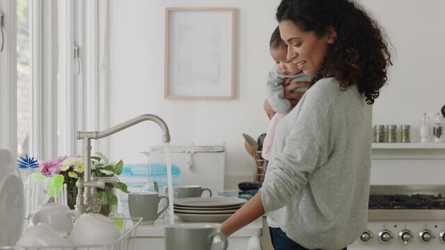 happy mother holding baby working at home washing dishes cleaning kitchen caring for toddler doing housework enjoying motherhood