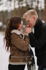 A happy married couple in love is hiding under a plaid blanket, warming up while walking traveling in the winter forest in nature in cold weather, selective focus