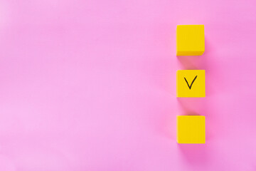 Three yellow cubes with a tick on one on pink. Copy space. Concept of choosing a better option,...