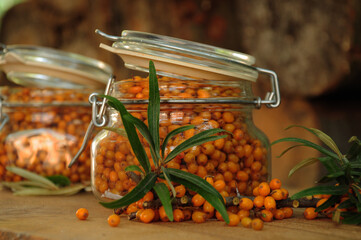 Ripe sea buckthorn berries with green leaves in a glass jar on a wooden board.
Sea buckthorn...